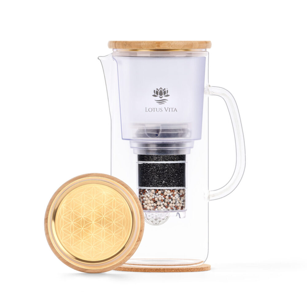 Glas-Wasserfilterkanne mit sichtbaren Filter-Schichten und einem Bambus-Deckel, daneben ein goldener Deckel mit eingraviertem Lebensblume-Muster.